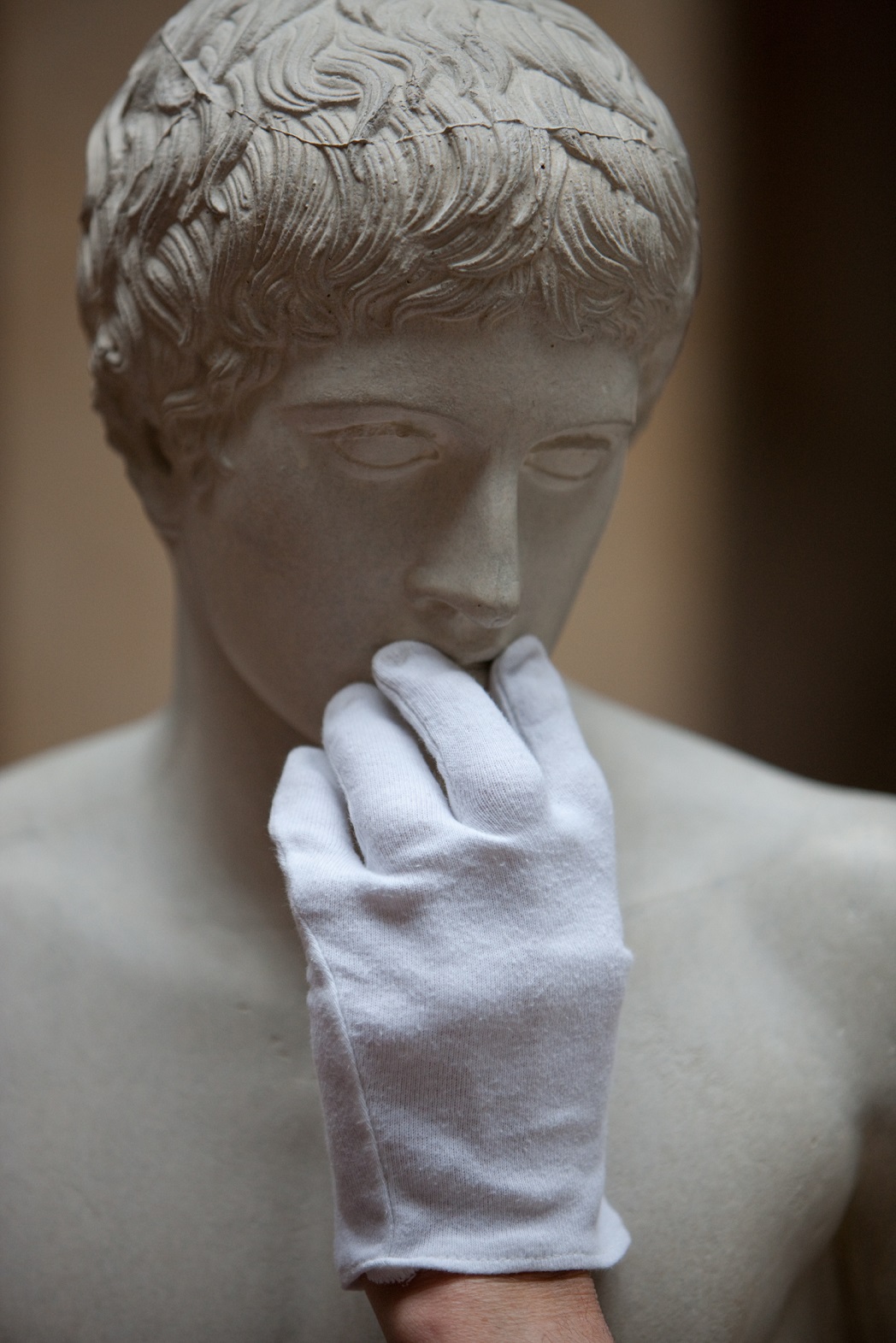 Eine behandschuhte Hand ertastet das Gesicht einer antiken Statue